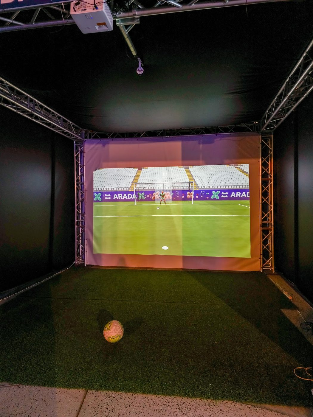 The penalty shootout installation: a football on artificial turf in front of a projection screen showing an ARADA-branded stadium goal.
