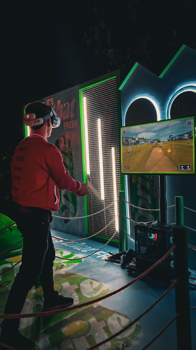 A player in a VR headset playing a shot at a Sprite-branded activation, with the in-game cricket pitch on a screen alongside.
